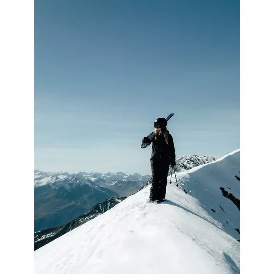 A skier standing on a snowy ridge at dusk