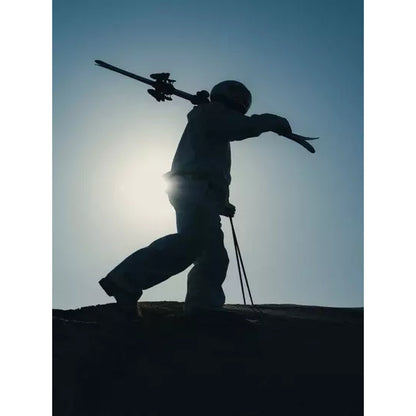 A skier silhouetted on a ridge at dusk, skis over one shoulder